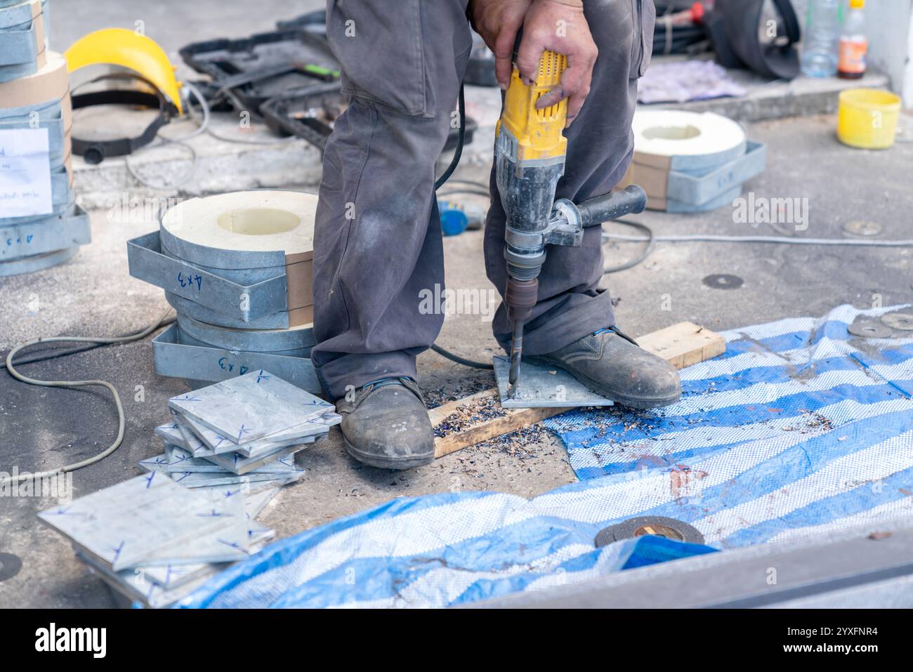 Le technicien utilise une perceuse pour percer des trous dans la plaque d'acier qui sera utilisée pour installer les poteaux en atelier. Banque D'Images