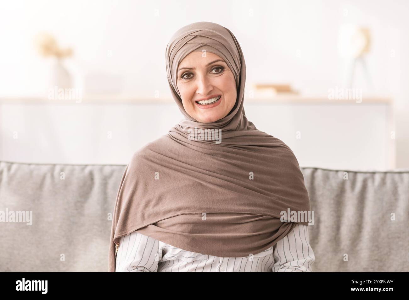 Femme musulmane sénior portant le hijab beige assis à la maison Banque D'Images