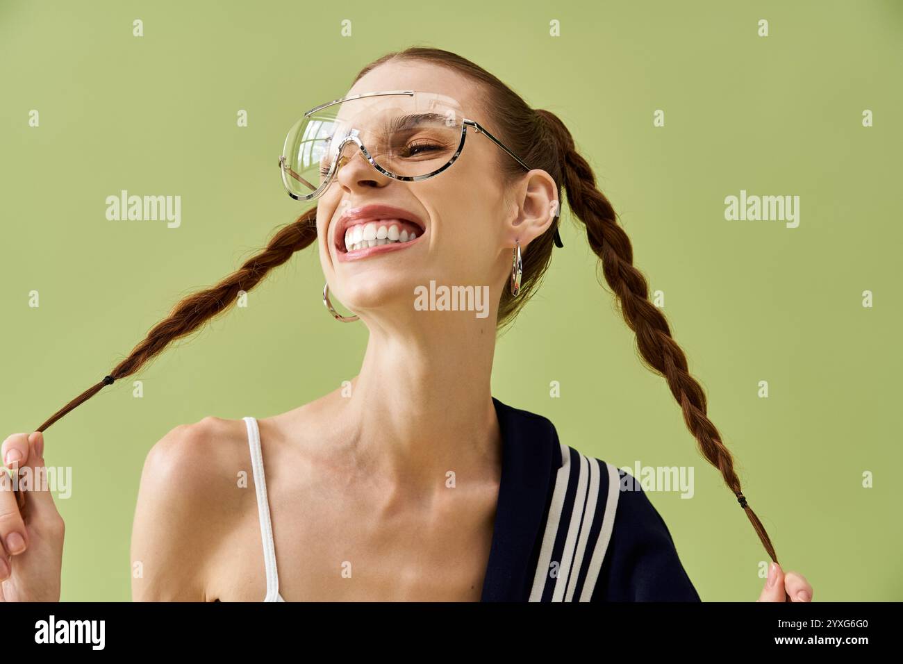Une jeune femme avec des tresses exprime la joie en souriant largement sur un fond vert vibrant. Banque D'Images