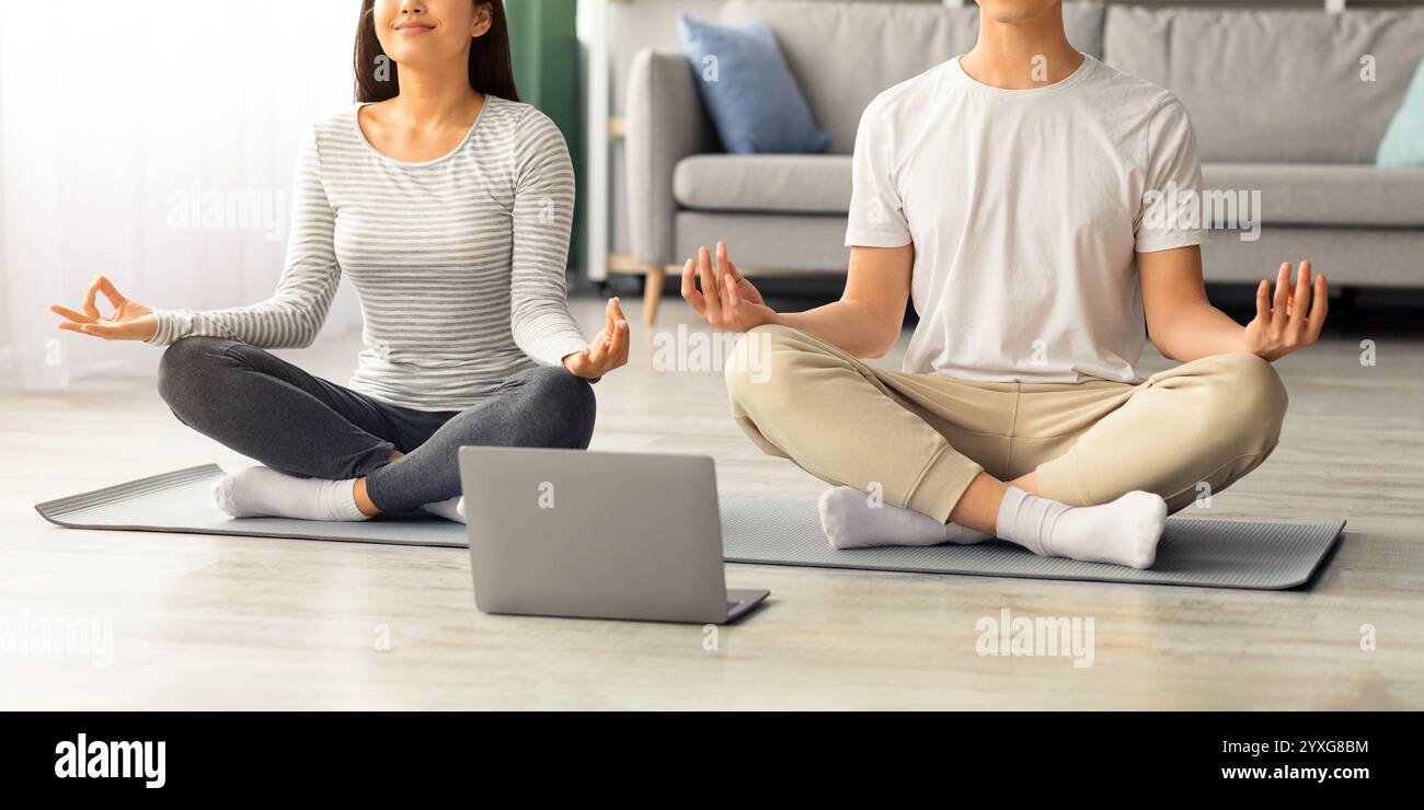 Paisible famille asiatique pratiquant la méditation à la maison, en utilisant un ordinateur portable Banque D'Images