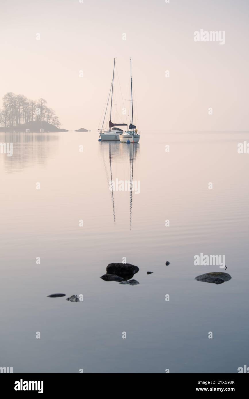 Deux yachts reflétant dans un lac calme avec un beau fond minimaliste brumeux. Windermere, Lake District, Royaume-Uni. Banque D'Images