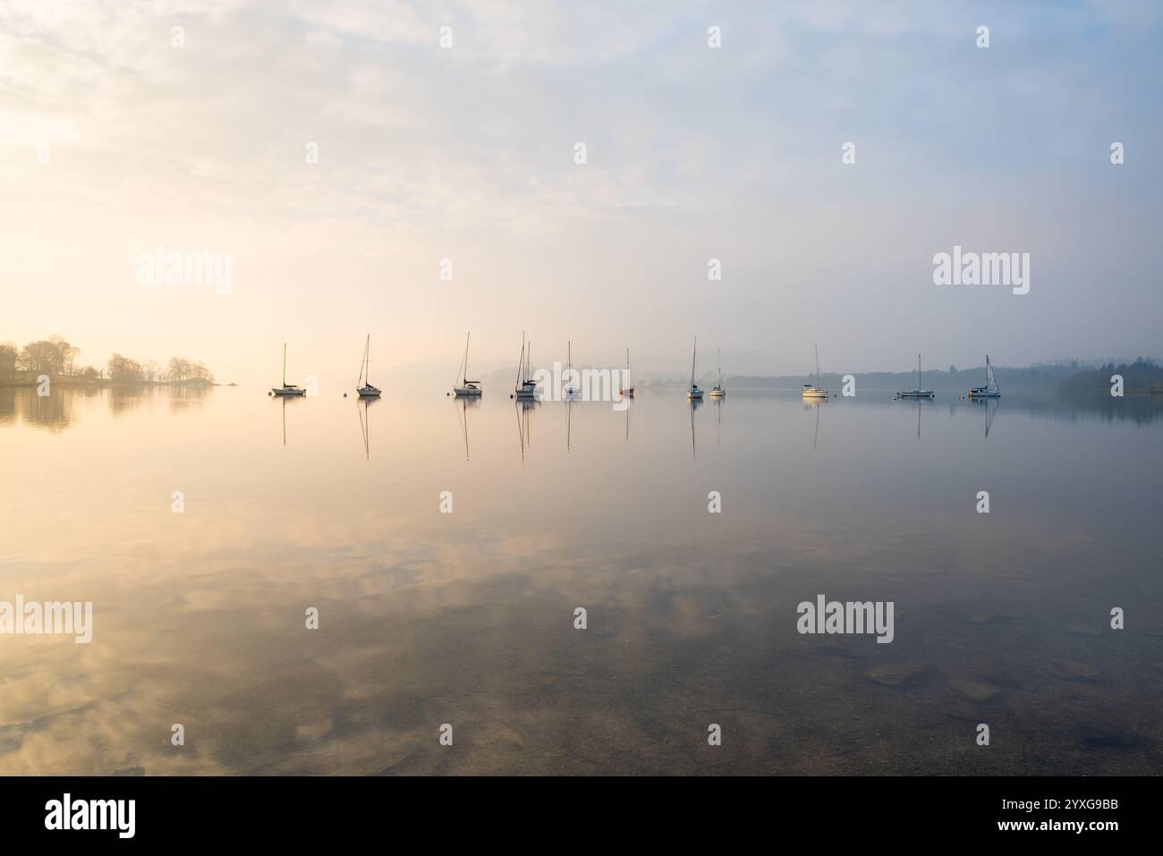 Rangée de bateaux reflétant dans le lac calme sur un matin brumeux à Windermere dans le Lake District, Royaume-Uni Banque D'Images