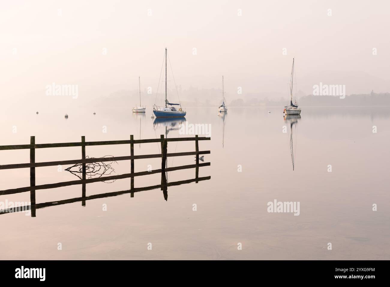 Belle matinée brumeuse calme avec des bateaux à voile reflétant dans le lac à Windermere dans le Lake District, Royaume-Uni. Banque D'Images