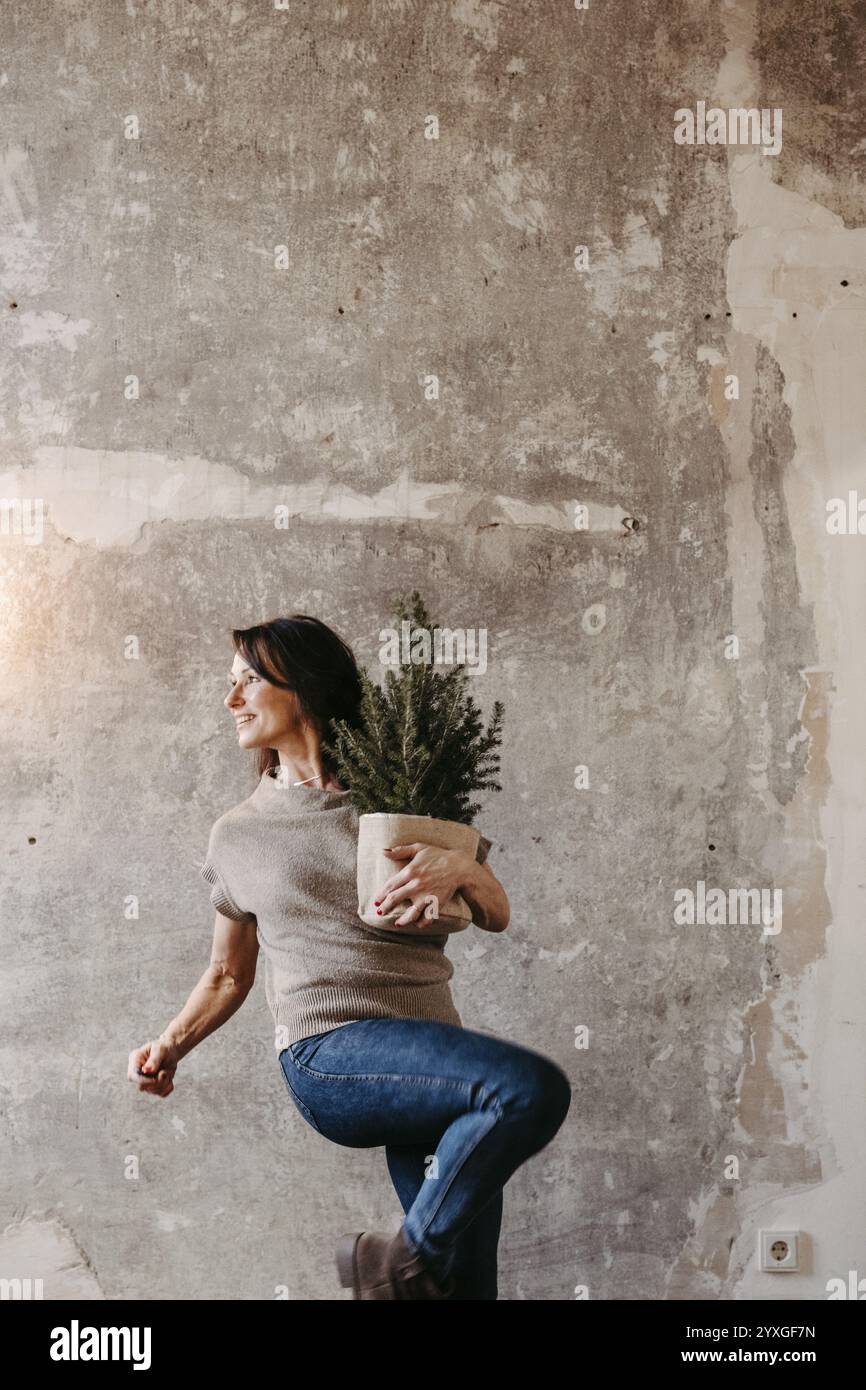 Femme dynamique devant un mur de béton gris avec un petit sapin de Noël à la main Banque D'Images