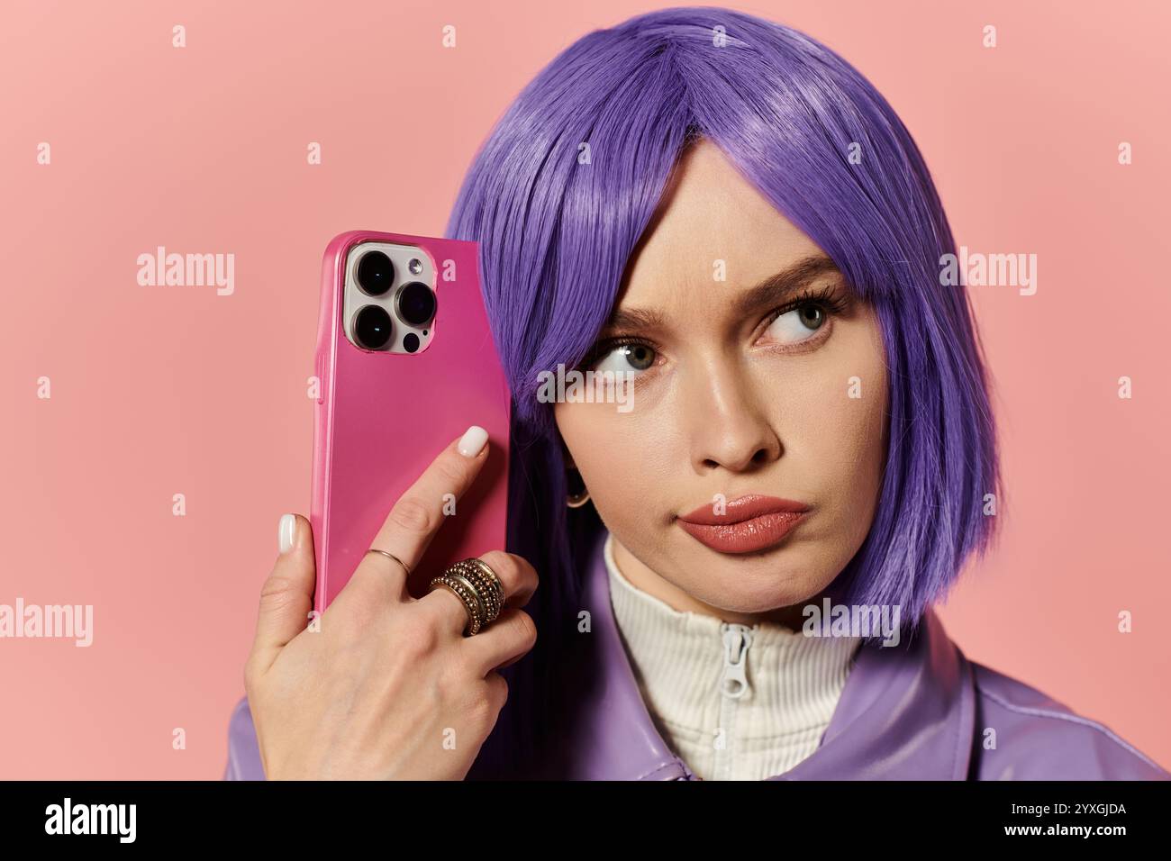 Une femme confiante avec une perruque violette met en valeur son style tout en tenant un téléphone rose. Banque D'Images