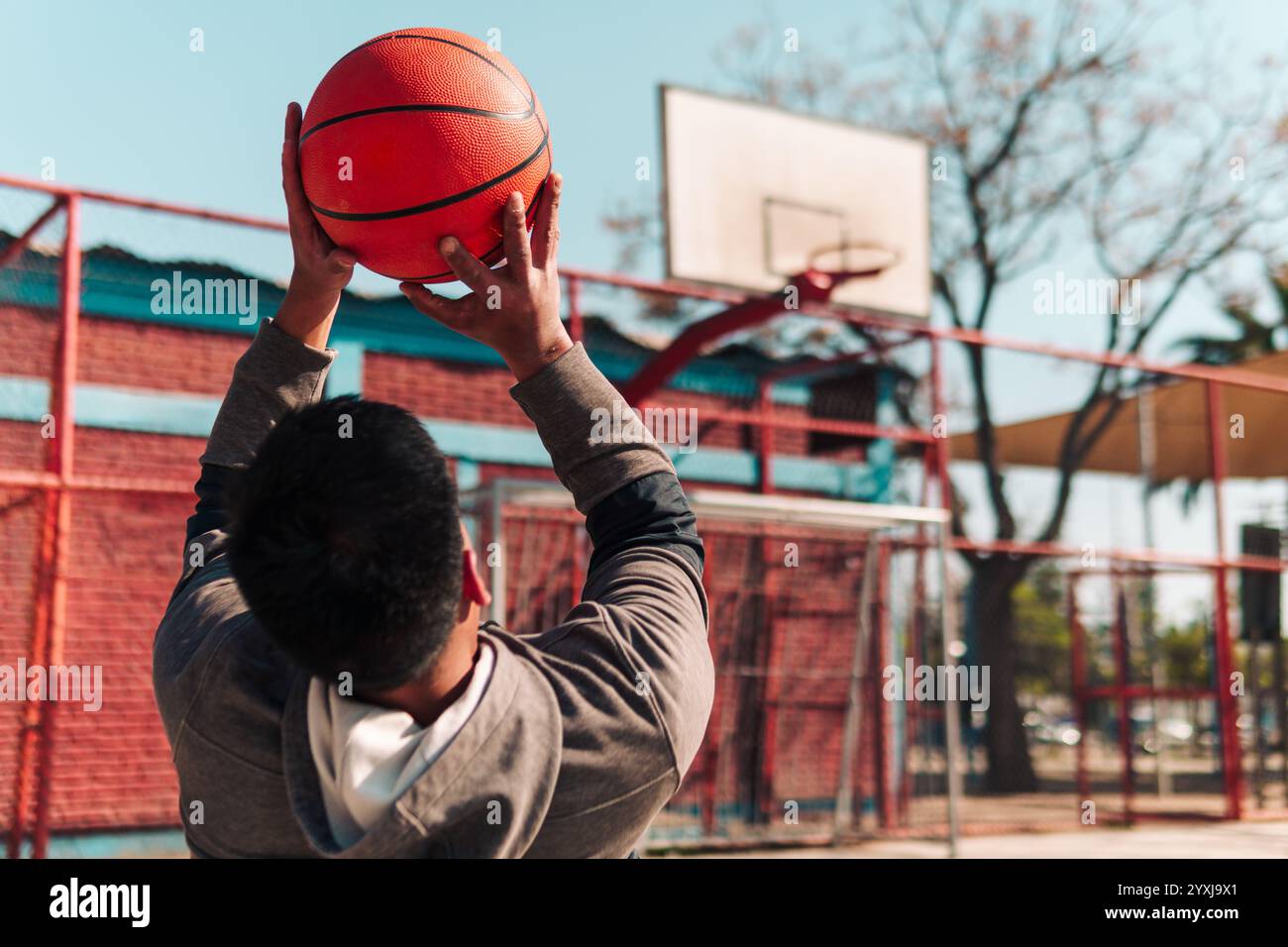 Jeune athlète latino en fauteuil roulant, s'entraînant, jouant et tirant au basket-ball dans un parc de la ville en plein air Banque D'Images