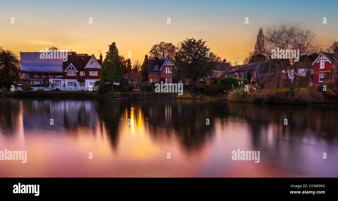 Maison traditionnelle anglaise reflétant sur un étang au coucher du soleil à Lindfield, West Sussex. Une longue exposition capture le charme serein du village. Banque D'Images