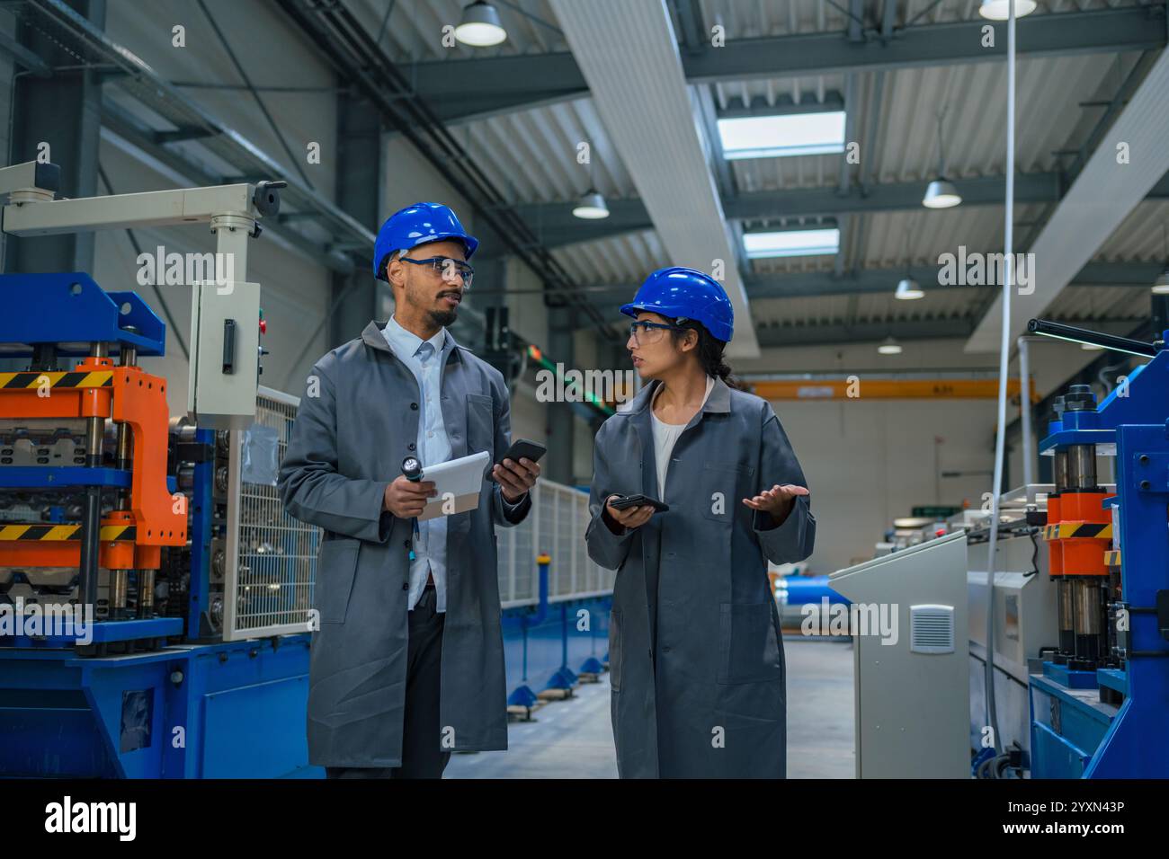 Deux ingénieurs, une indienne et un Afro-américain avec des casques bleus inspectant une machine en usine. Banque D'Images