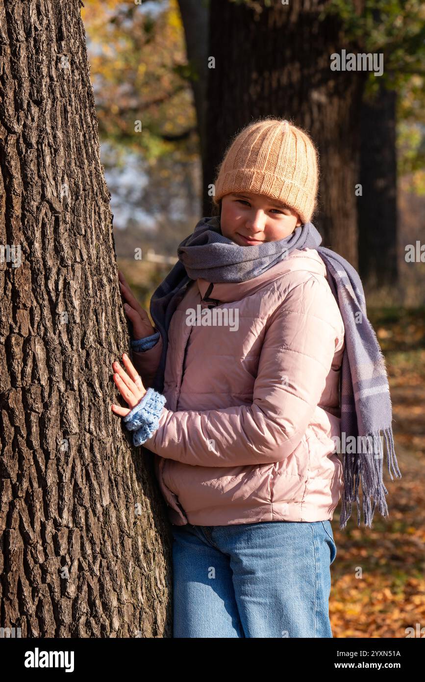 Fille souriante de 10 ans profitant du temps d'automne, debout près d'un arbre avec des feuilles jaunes. Promenades actives en plein air. Banque D'Images