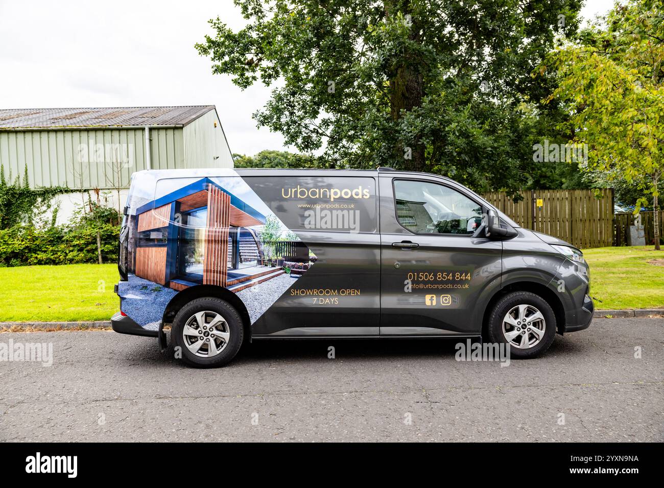 Une fourgonnette Ford transit Custom gris foncé est garée sur de l'asphalte, avec une enveloppe partielle avec une photo sur le côté d'un pod House urbain et les coordonnées Banque D'Images