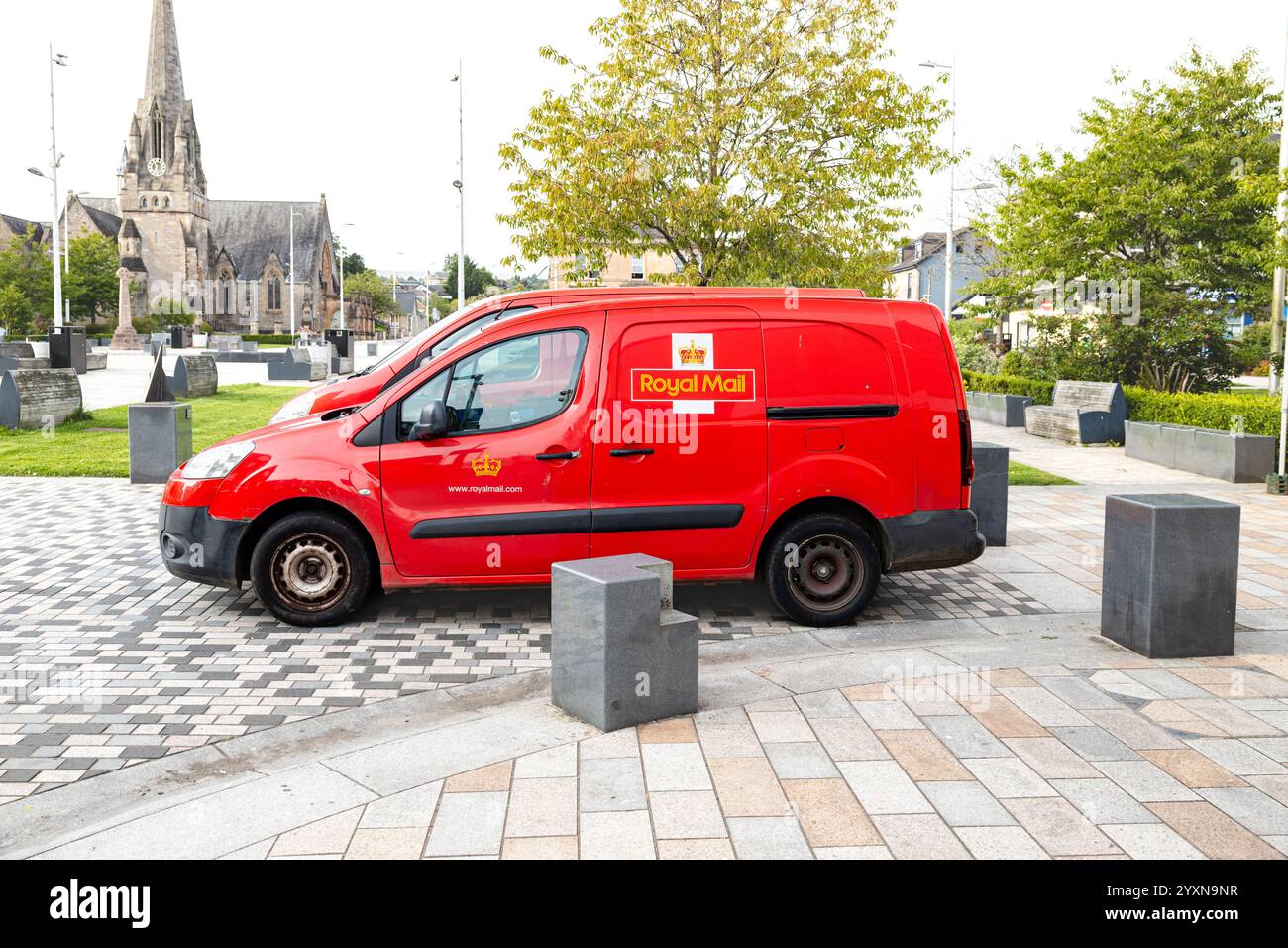 Garé Red Royal mail Van, avec un deuxième van derrière. Le logo, Crown et Royal mail et l'URL sont clairement visibles. Église et autre vie de ville derrière Banque D'Images