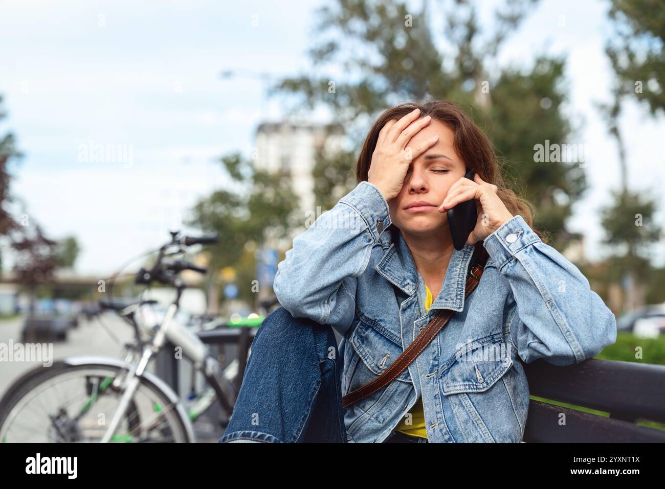 Femme caucasienne déçue parlant téléphone tout en étant assise sur le banc de la rue. Banque D'Images