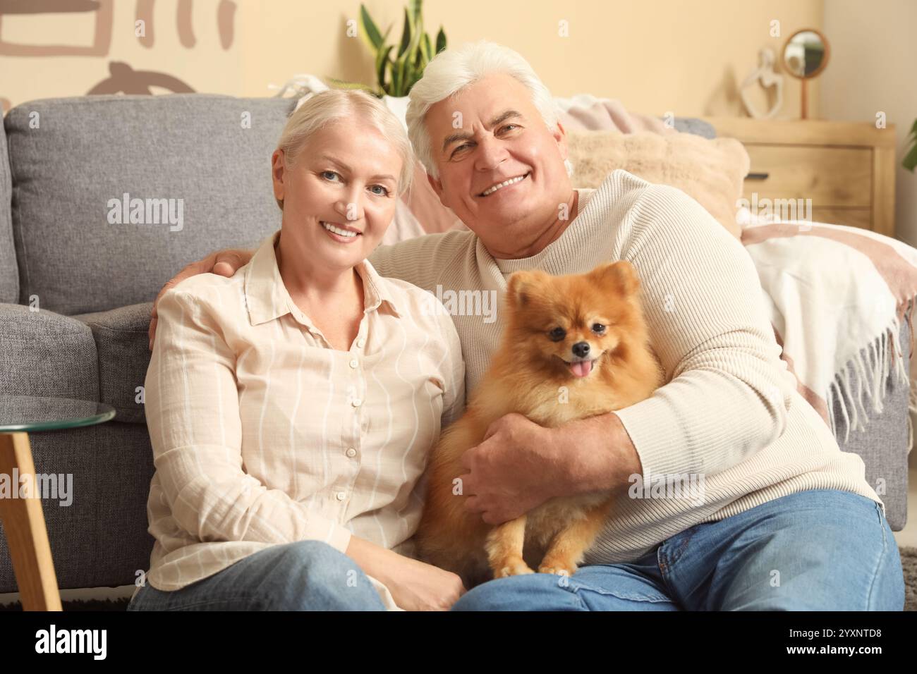 Heureux couple aîné avec chien pomeranian mignon assis sur le sol à la maison Banque D'Images