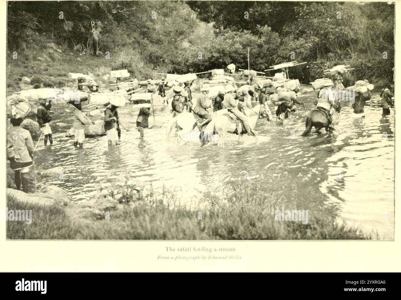 African Game Trails, 1910, chasse, Ouganda, description et voyage, Afrique de l'est, dans cette scène, un groupe de personnes patère dans une rivière, portant diligemment de lourdes charges sur le dos. L'eau reflète la végétation luxuriante environnante et le contour lointain d'une colonie peut être vu le long de la rive. Les individus sont vus naviguer dans le courant, faisant preuve de détermination et de résilience dans leur tâche. L'atmosphère dégage un sentiment de communauté lorsqu'ils travaillent ensemble, illustrant le travail acharné impliqué dans le transport de marchandises à travers un paysage naturel. Banque D'Images