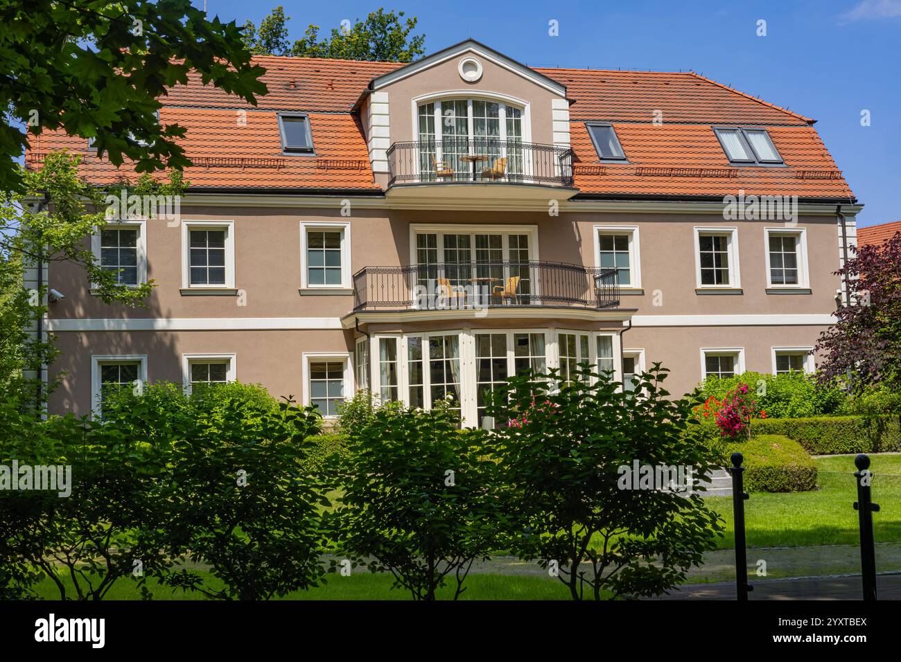 Élégante villa de luxe avec façade beige, toit en tuiles rouges et balcons entourés d'un jardin verdoyant et d'arbres luxuriants. Banque D'Images
