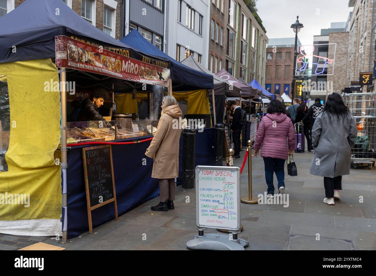 Londres, Royaume-Uni - 3 décembre 2024, Une femme achète du kebab de poulet à un vendeur dans un marché de Street food vendant de la cuisine libanaise. Banque D'Images