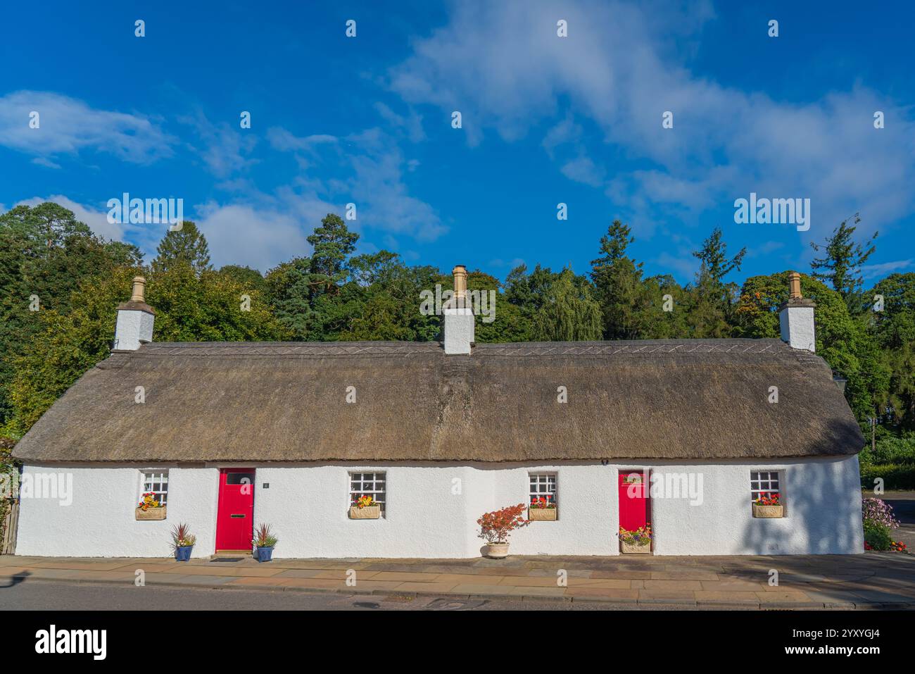 Glamis, Écosse - septembre 2024 : une vieille maison blanche avec un toit de chaume et des portes rouges Banque D'Images