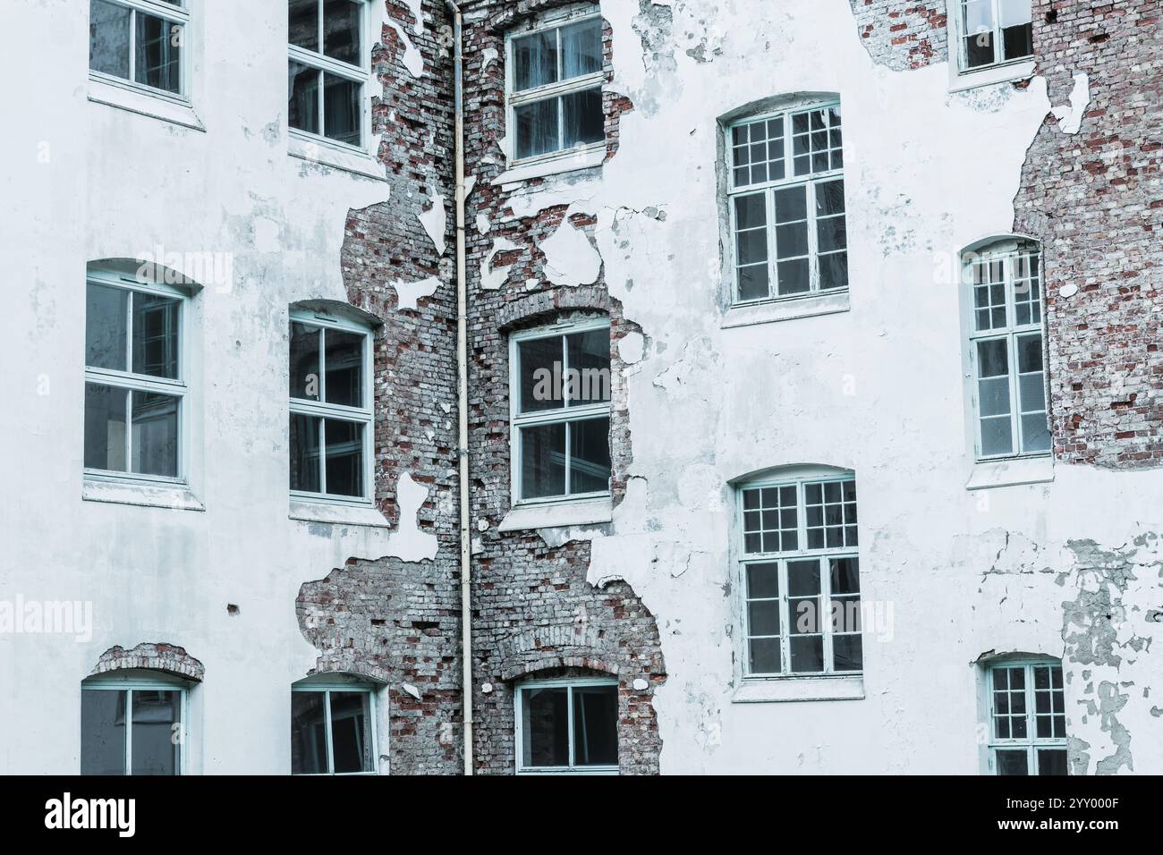 Le sanatorium abandonné révèle des murs de briques en ruine avec de la peinture blanche écaillée et des fenêtres brisées, mettant en valeur le passage du temps et la négligence dans un havre Banque D'Images