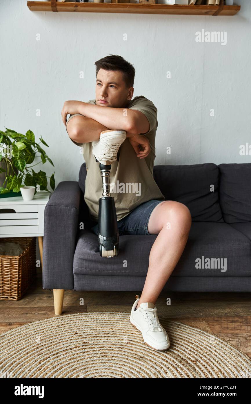 Un beau jeune homme est assis confortablement sur un canapé, embrassant sa jambe avec une prothèse. Banque D'Images