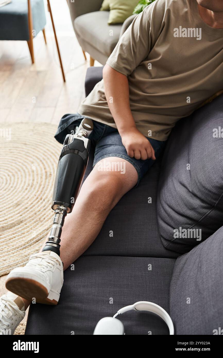 Beau jeune homme est assis confortablement sur un canapé, mettant en valeur sa jambe prothétique tout en se relaxant. Banque D'Images