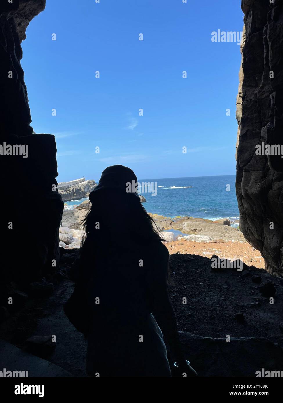 silhouette sombre de femme célibataire dans une grotte avec un ciel bleu et un fond d'océan - Image de stock capturée avec un smartphone