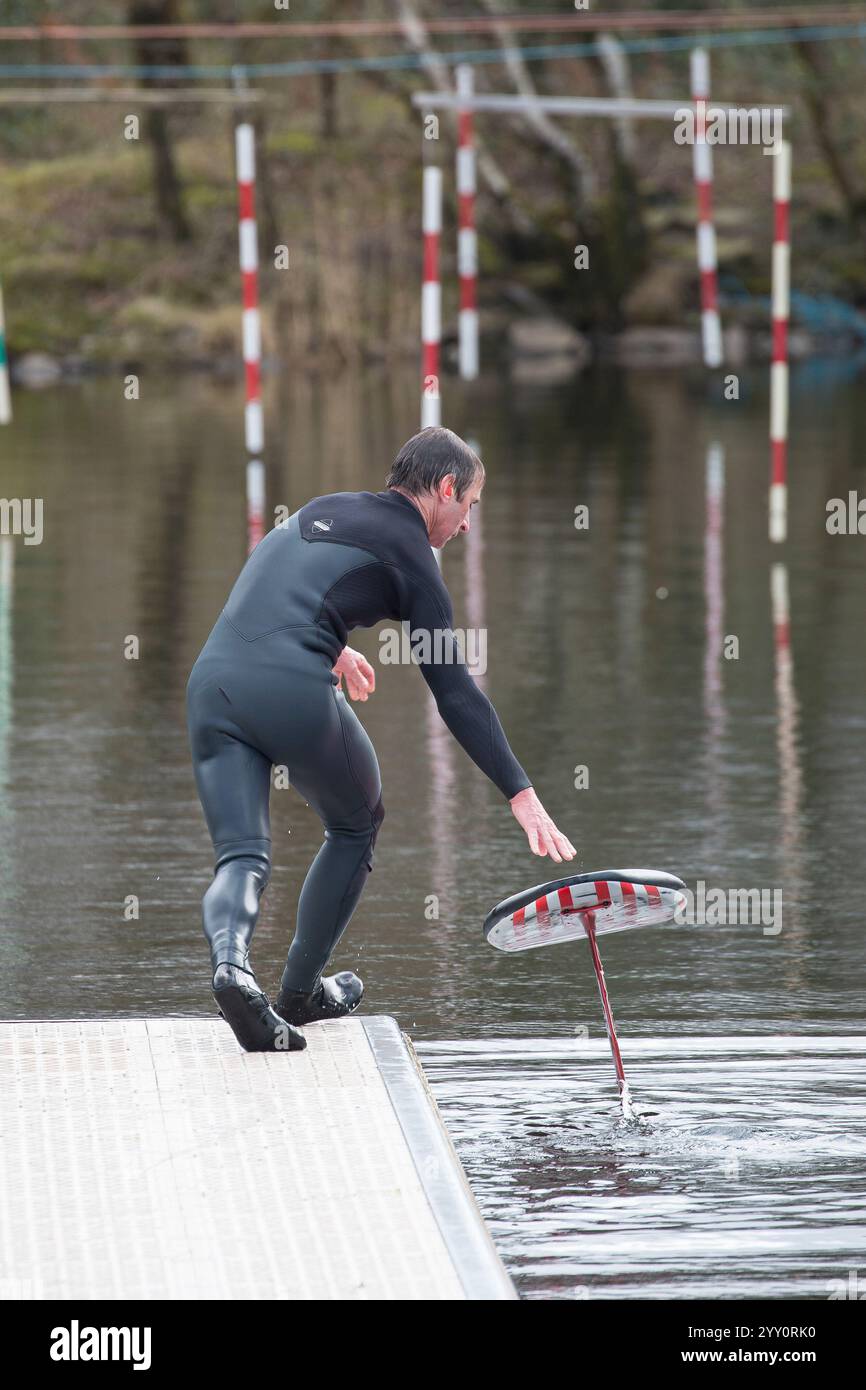 Vue arrière d'un homme portant une combinaison lançant une planche d'hydroptère sur un lac au pays de Galles. Banque D'Images