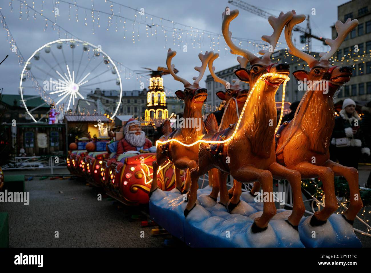 Un carrousel pour enfants avec des rennes est visible sur les marchés de Noël de Poznan (Betlejem Pozna?skie) sur la place de la liberté dans le centre de Poznan le dimanche soir, avec une grande roue en arrière-plan. Pozna ? Marchés de Noël (Betlejem Pozna?skie) – une foire annuelle de Noël au cœur de Pozna?. L'atmosphère unique du marché de Noël est créée par des décorations et des illuminations festives, un sapin de Noël, une grande roue, un carrousel vénitien, et une scène de Noël présentant un répertoire artistique local, des événements thématiques le week-end et des ateliers pour les enfants. Banque D'Images