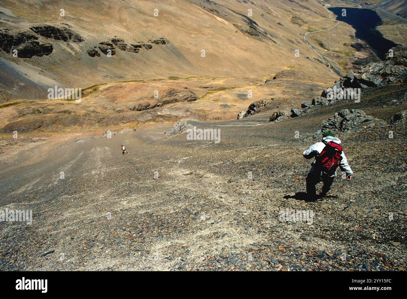 Randonneurs descendant une pente raide et rocheuse en Bolivie. Le paysage aride présente des montagnes escarpées et une rivière lointaine Banque D'Images