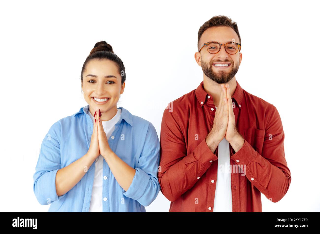 Souriant homme positif et femme avec les mains ensemble dans un geste de prière, exprimant la gratitude ou l'espoir, vêtus de façon désinvolte dans un short, se tiennent sur fond blanc isolé Banque D'Images