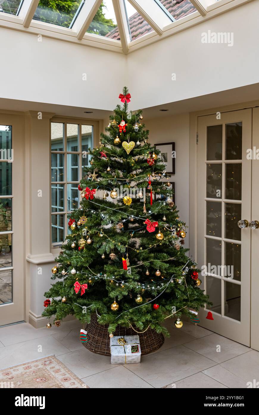 Intérieur de la maison avec arbre de Noël décoré et présent sous l'arbre dans le conservatoire du salon, Royaume-Uni Banque D'Images