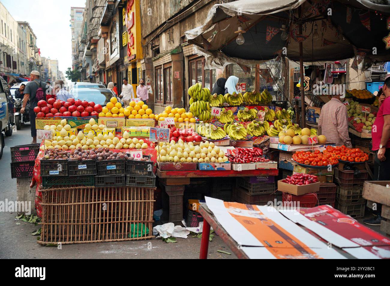 Un stand de fruits coloré à Alexandrie, Egypte, affichant des bananes mûres, des poires, des grenades, et des poivrons dans un cadre de marché traditionnel animé. Banque D'Images