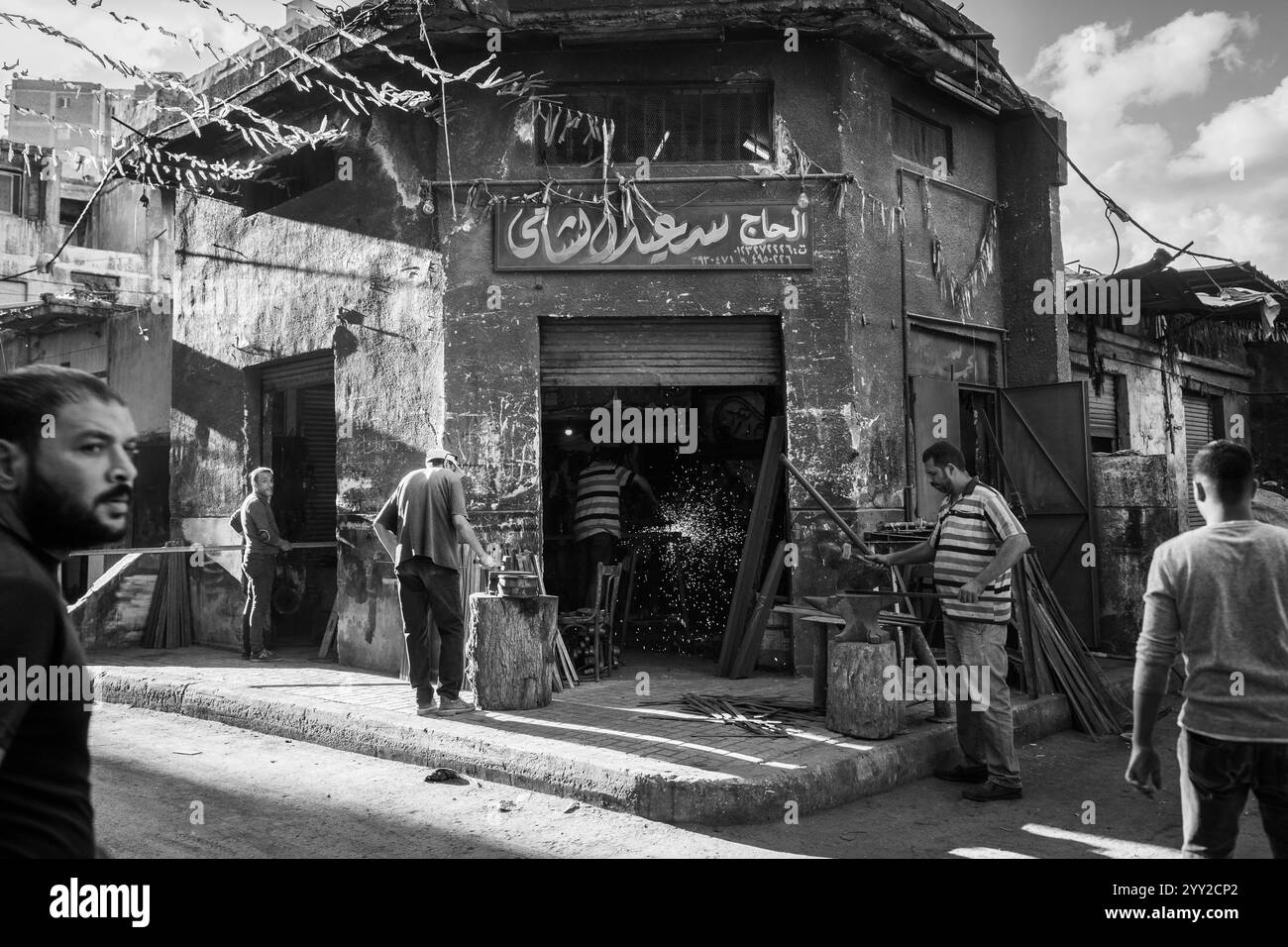 Un atelier de forgeron animé à Alexandrie, Egypte. Les ouvriers forgent le métal avec des étincelles volantes, incarnant l'artisanat traditionnel dans un cadre urbain. Banque D'Images