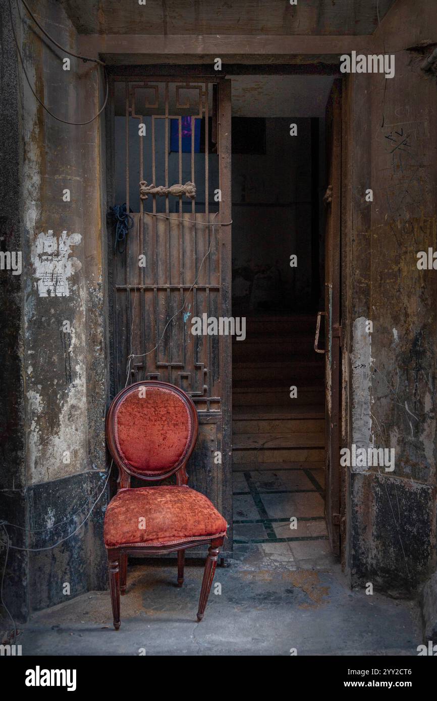 Une chaise en velours rouge altéré se trouve à l'extérieur d'une ancienne porte rustique en fer à Alexandrie, en Égypte, évoquant une esthétique urbaine vintage. Banque D'Images