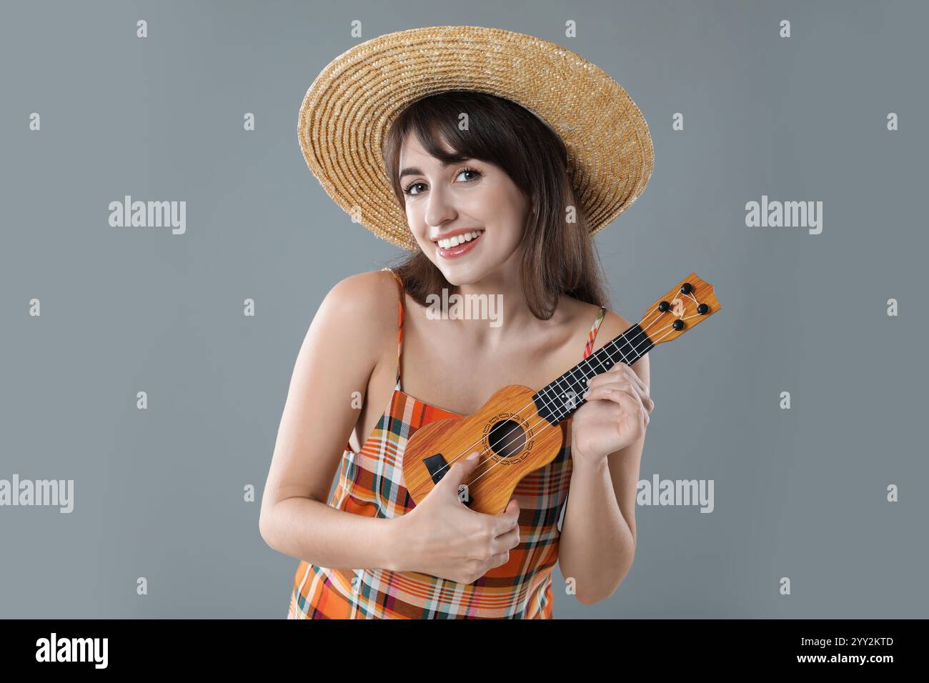 Femme heureuse jouant ukulélé sur fond gris Banque D'Images