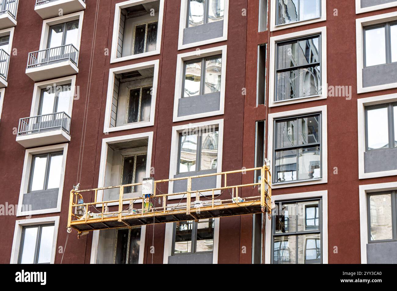 Échafaudage de construction suspendu devant une façade de bâtiment moderne avec des fenêtres, mettant en valeur des travaux de rénovation extérieurs Banque D'Images