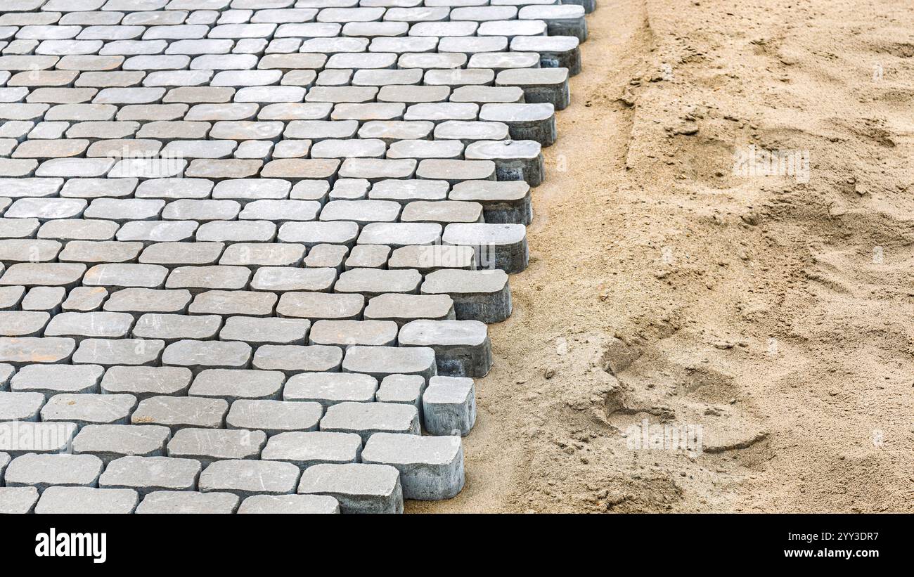 Pavés posés sur une base de sable, montrant le détail des travaux de pavage non finis. Concept de construction et de terrassement Banque D'Images