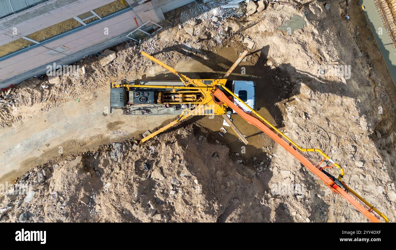 Vue aérienne d'un chantier de construction avec un camion-pompe à béton étendant son bras de flèche sur une zone de terre à côté d'un bâtiment. Banque D'Images