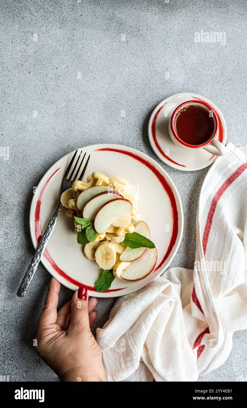 Gaufres recadrées méconnaissables, garnies de pommes, de bananes et de menthe servies avec une tasse de café, vues d'en haut. Banque D'Images