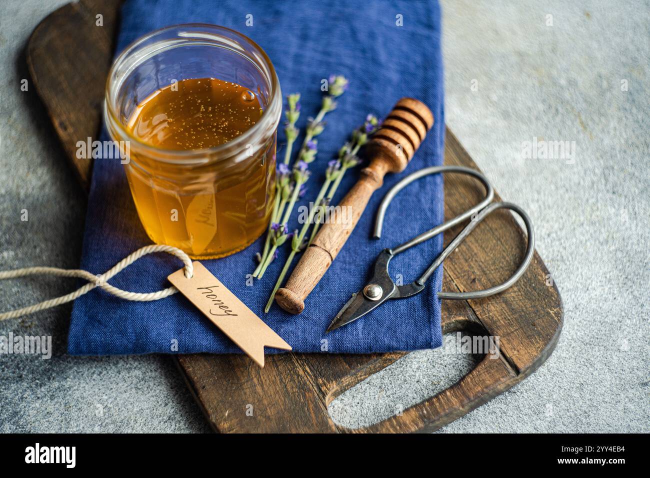 Un arrangement confortable mettant en vedette un pot de miel doré, des brins de lavande et des outils rustiques sur une planche de bois le tissu bleu foncé ajoute une touche d'élégance Banque D'Images
