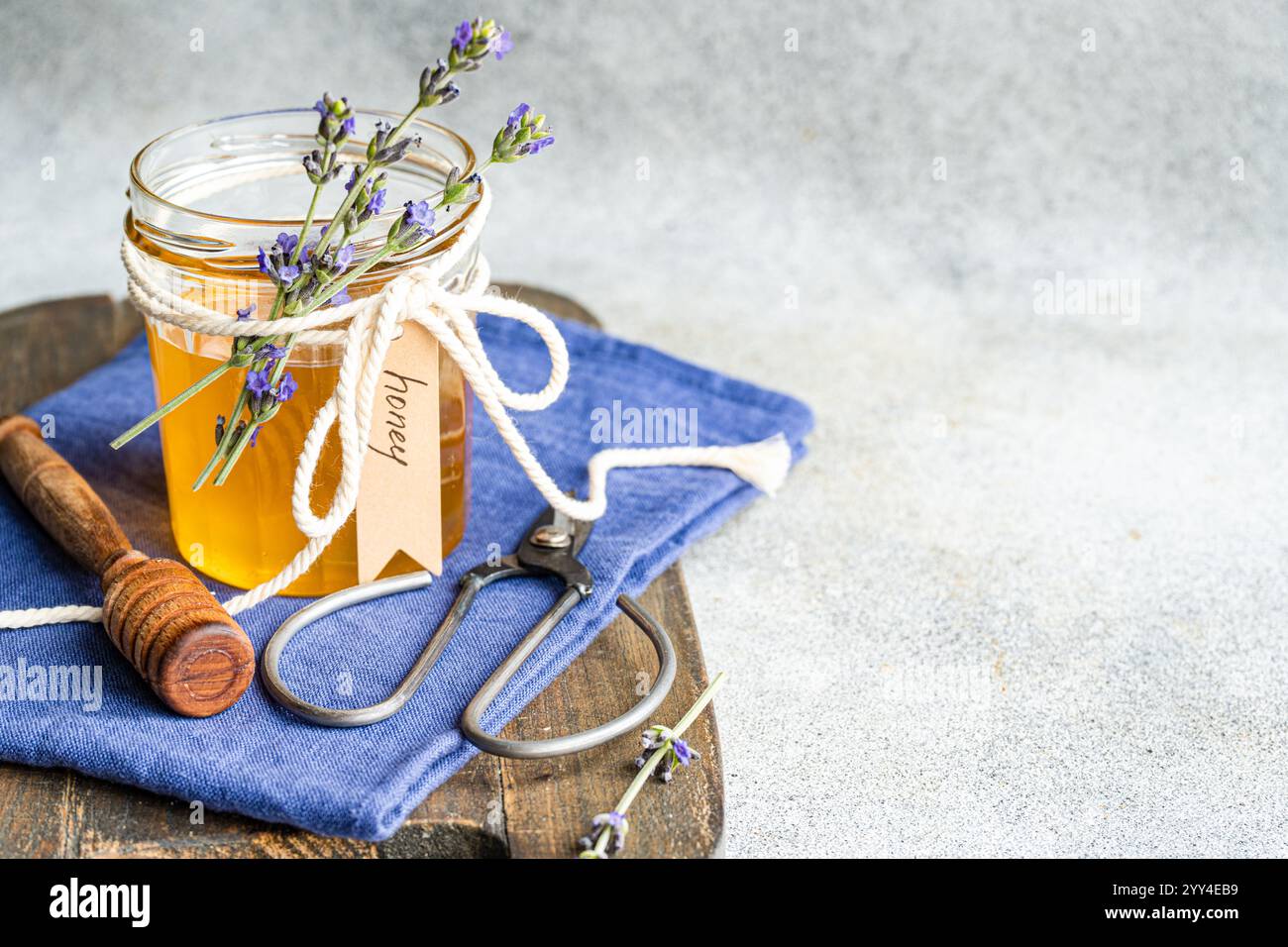Un pot en verre rempli de miel, décoré de brins de lavande attachés avec une corde blanche le cadre comprend une trempette à miel, des ciseaux vintage et un c bleu Banque D'Images