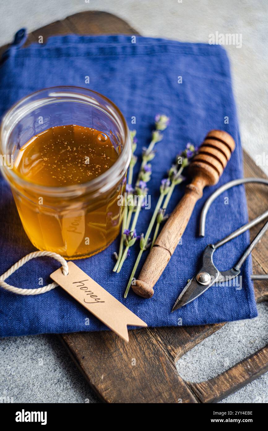 Un pot de miel doré avec une trempette en bois rustique et de délicats brins de lavande repose sur une serviette bleue la configuration évoque un th aromatique naturel et doux Banque D'Images