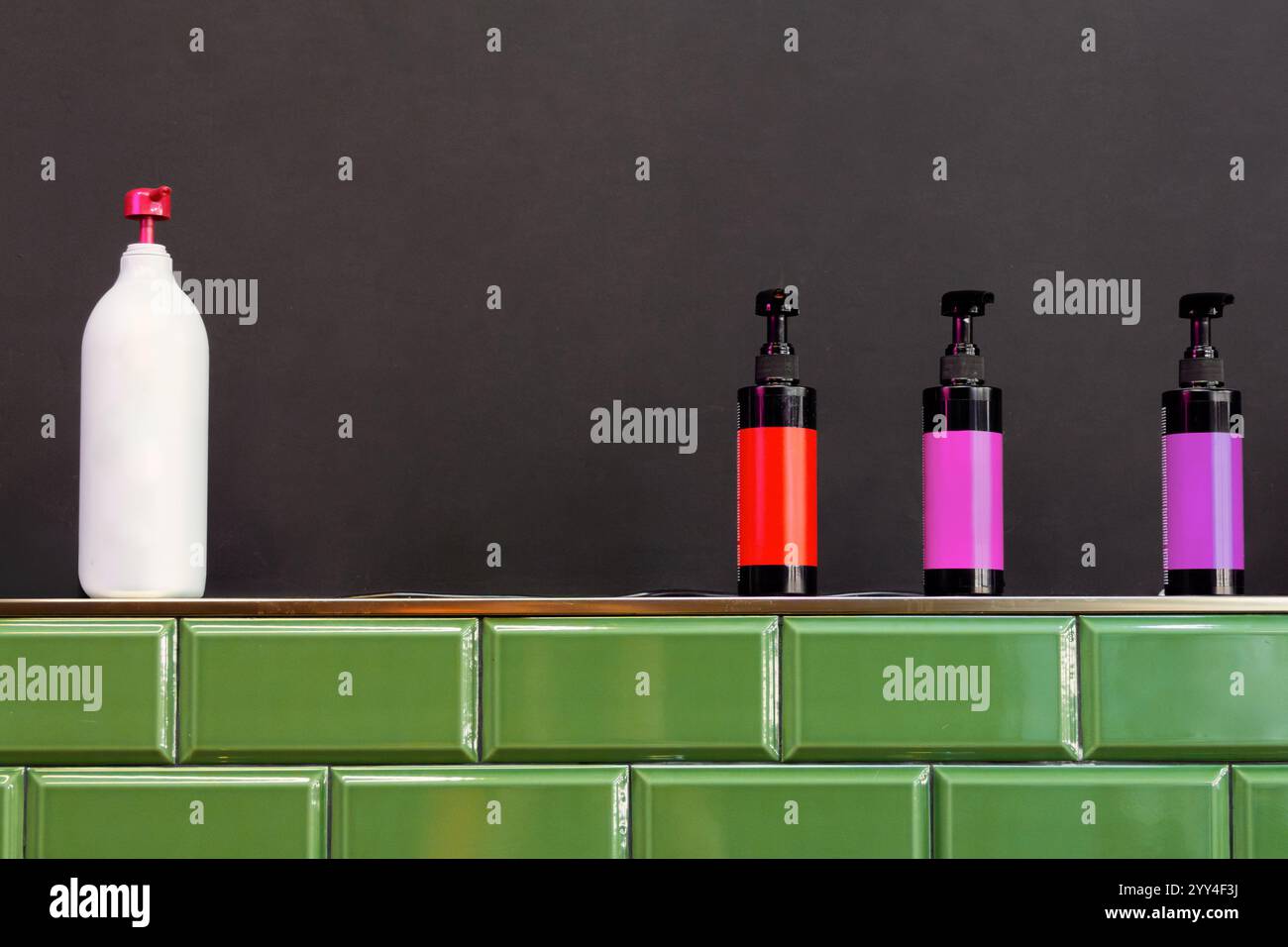 Les bouteilles colorées de produits capillaires sont soigneusement disposées sur un comptoir élégant et carrelé de vert sur un fond sombre, capturant l'essence d'un salon de cheveux moderne Banque D'Images