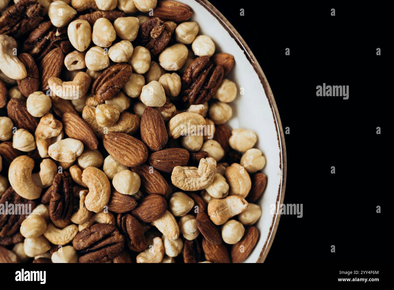 Un délicieux assortiment de noix mélangées, y compris des amandes, des pacanes, des noisettes et des noix de cajou dans un bol décoratif sur un fond sombre parfait pour les saines Banque D'Images