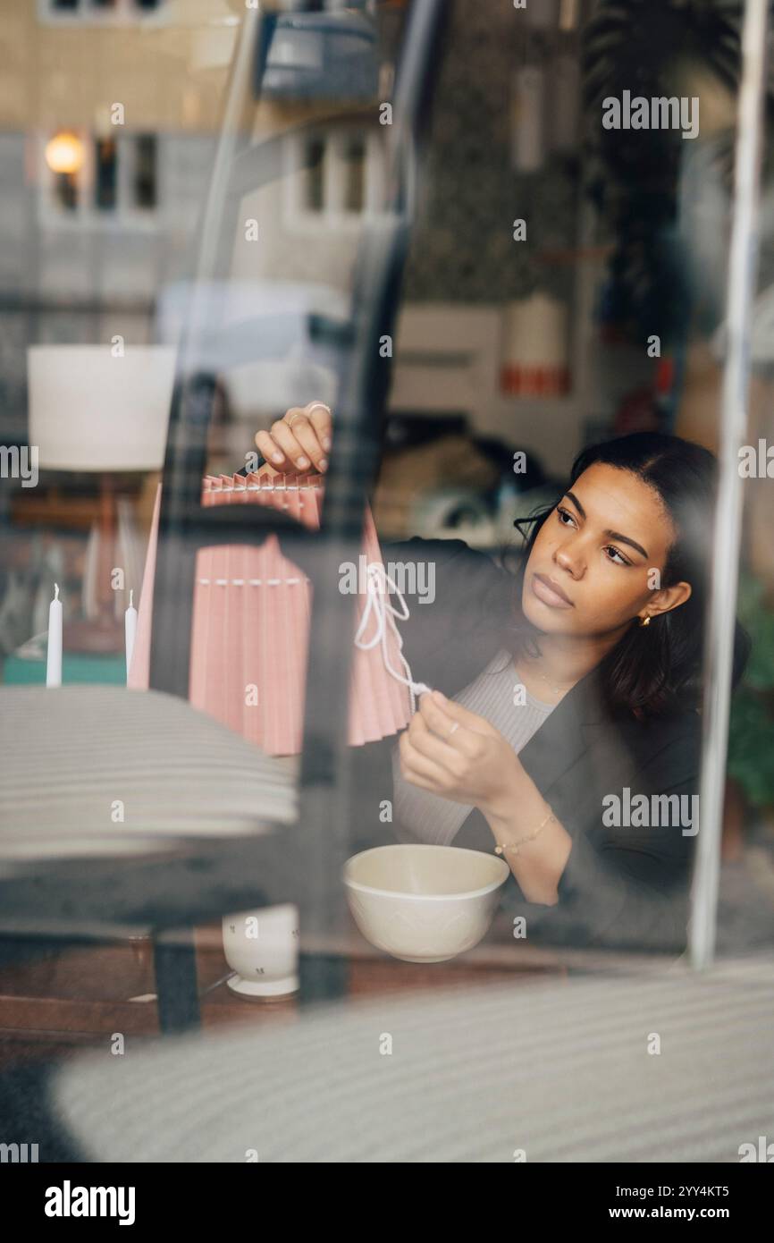 Jeune femme entrepreneure ajustant l'abat-jour tout en travaillant au magasin d'antiquités Banque D'Images