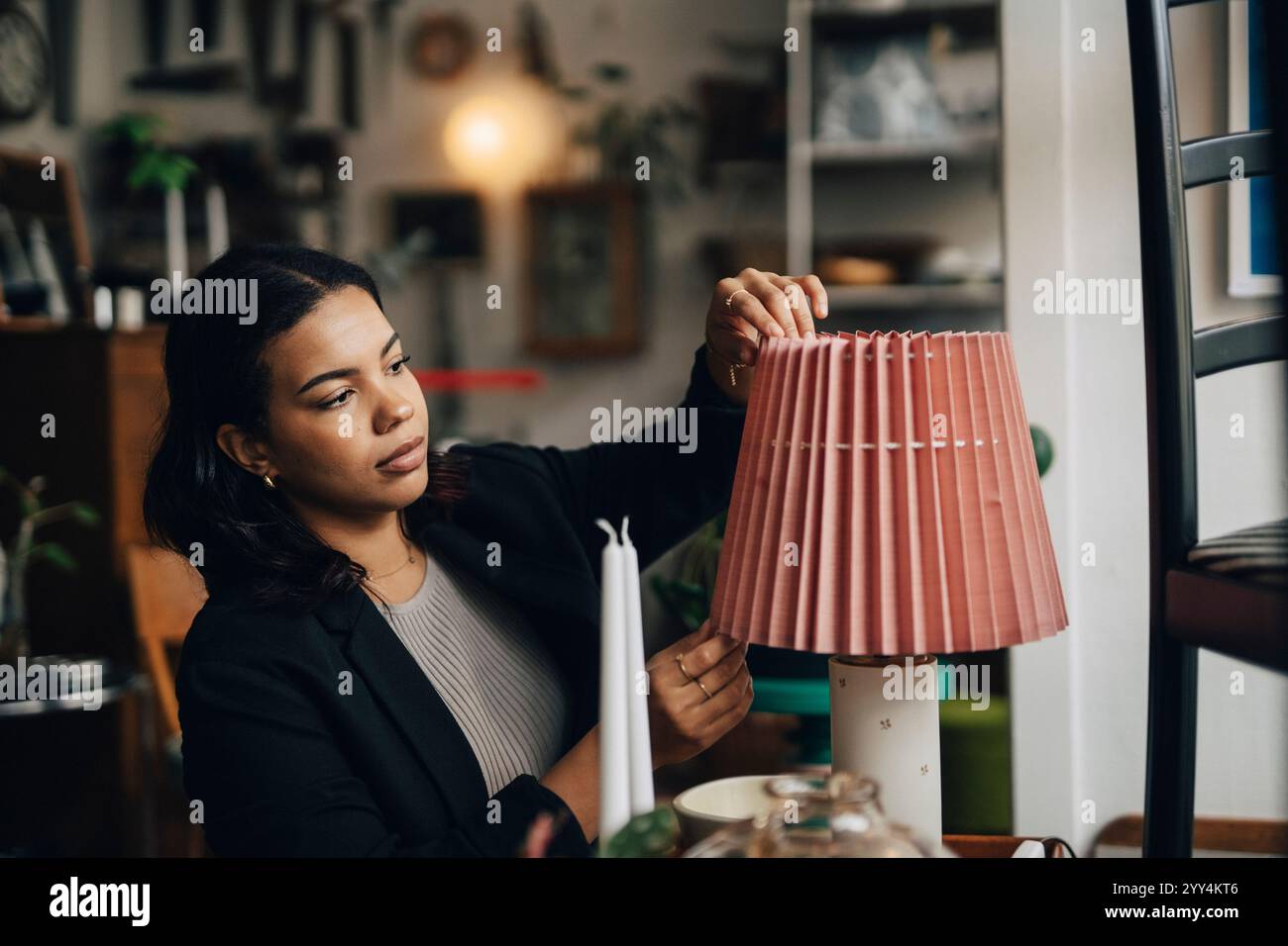 Jeune femme entrepreneure ajustant l'abat-jour tout en travaillant au magasin d'antiquités Banque D'Images
