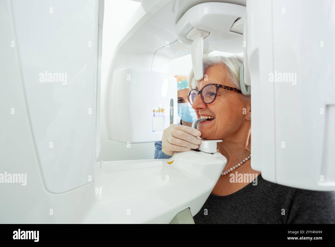 Dentiste ajustant la machine à rayons X panoramique tout en fournissant des soins à une femme âgée dans une clinique dentaire moderne axée sur la santé bucco-dentaire Banque D'Images
