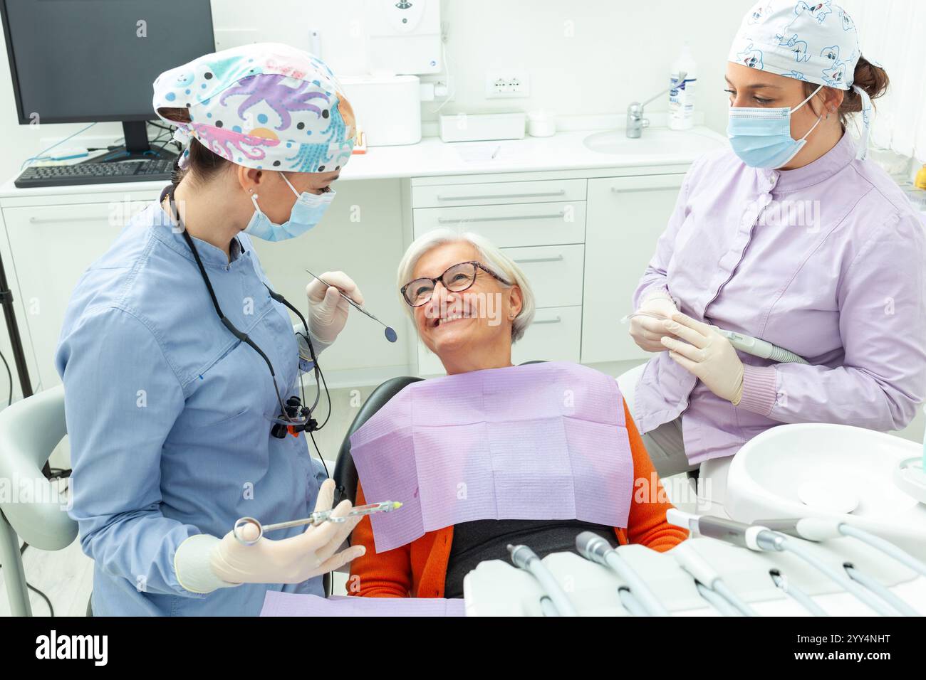 Deux dentistes préparant une femme âgée pour une intervention dentaire à venir, assurant confort et soins dans un cadre de clinique dentaire moderne Banque D'Images