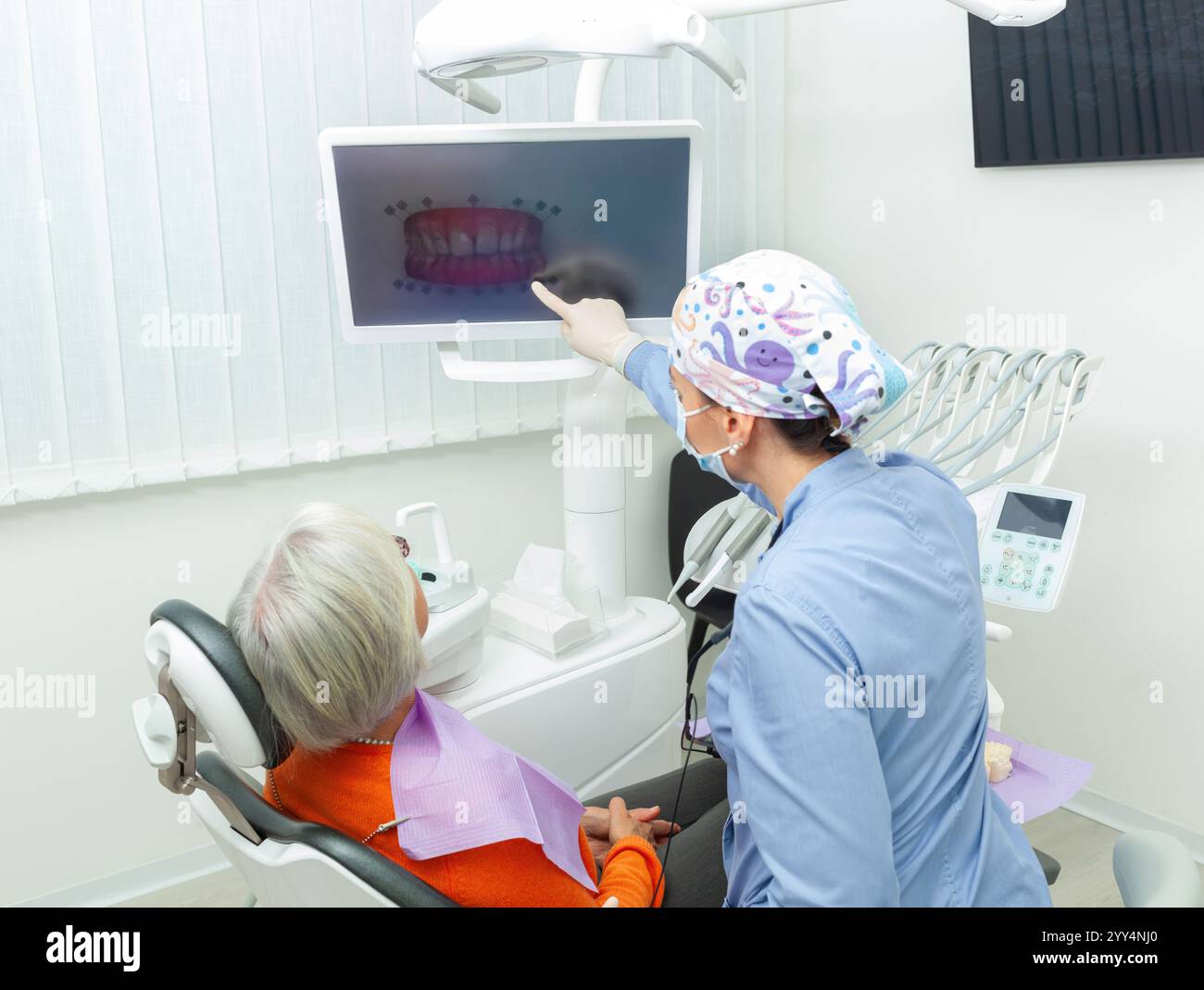Dentiste pointant vers un moniteur affichant une radiographie des dents tout en consultant un patient âgé dans une clinique dentaire moderne Banque D'Images