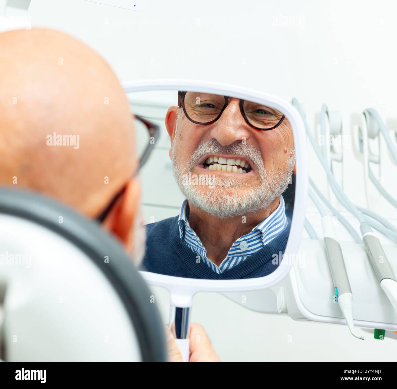 Homme senior vérifiant ses nouvelles dents dans le miroir à la clinique dentaire, heureux avec le résultat de la chirurgie de l'implant dentaire Banque D'Images