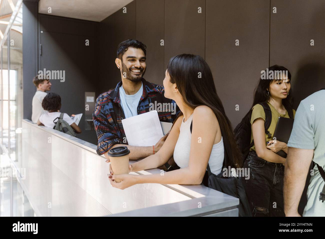 Heureux étudiant universitaire masculin parlant avec une amie féminine tout en se tenant debout dans le couloir du collège Banque D'Images Heureux étudiant universitaire masculin parlant avec une amie féminine tout en se tenant debout dans le couloir du collège Banque D'Images